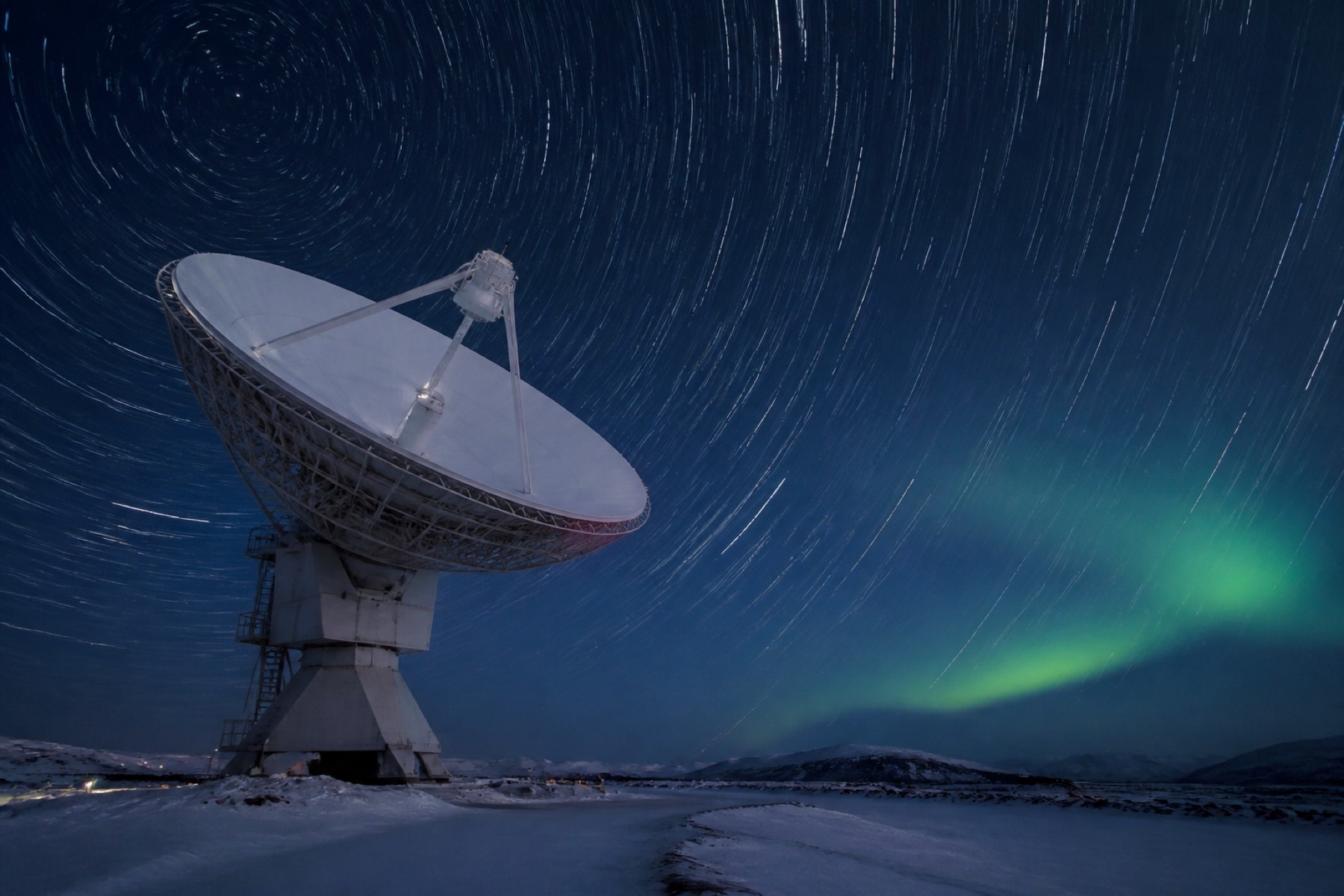 Grande antenne parabolique de station sol sous un ciel étoilé et une aurore boréale